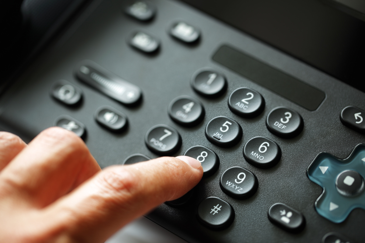 A close up on a phone keypad, with a ring finger extended out towards the eight dial.