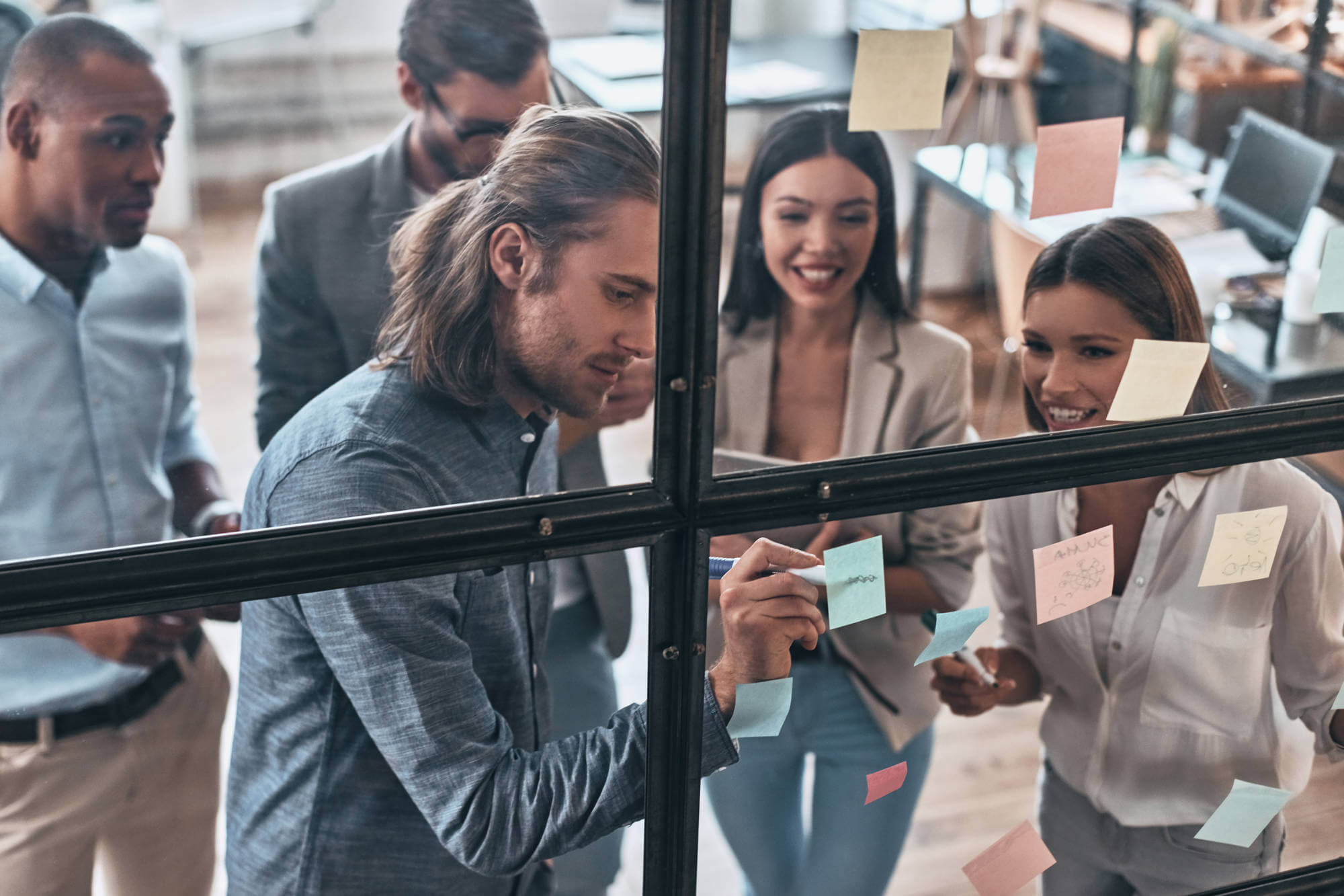 Young professionals in business casual wear writing on adhesive notes against a glass wall