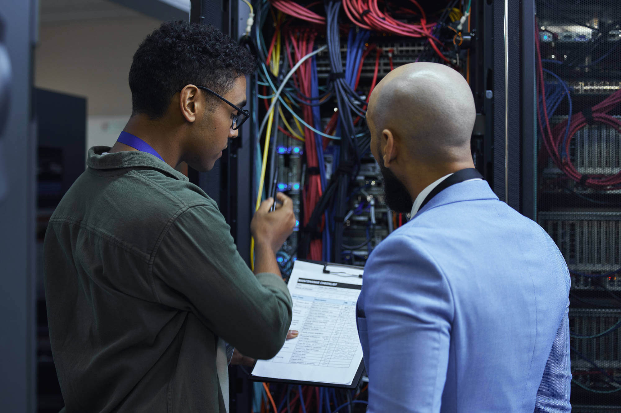 Two male information technology (IT) support agents working together in a dark network server
